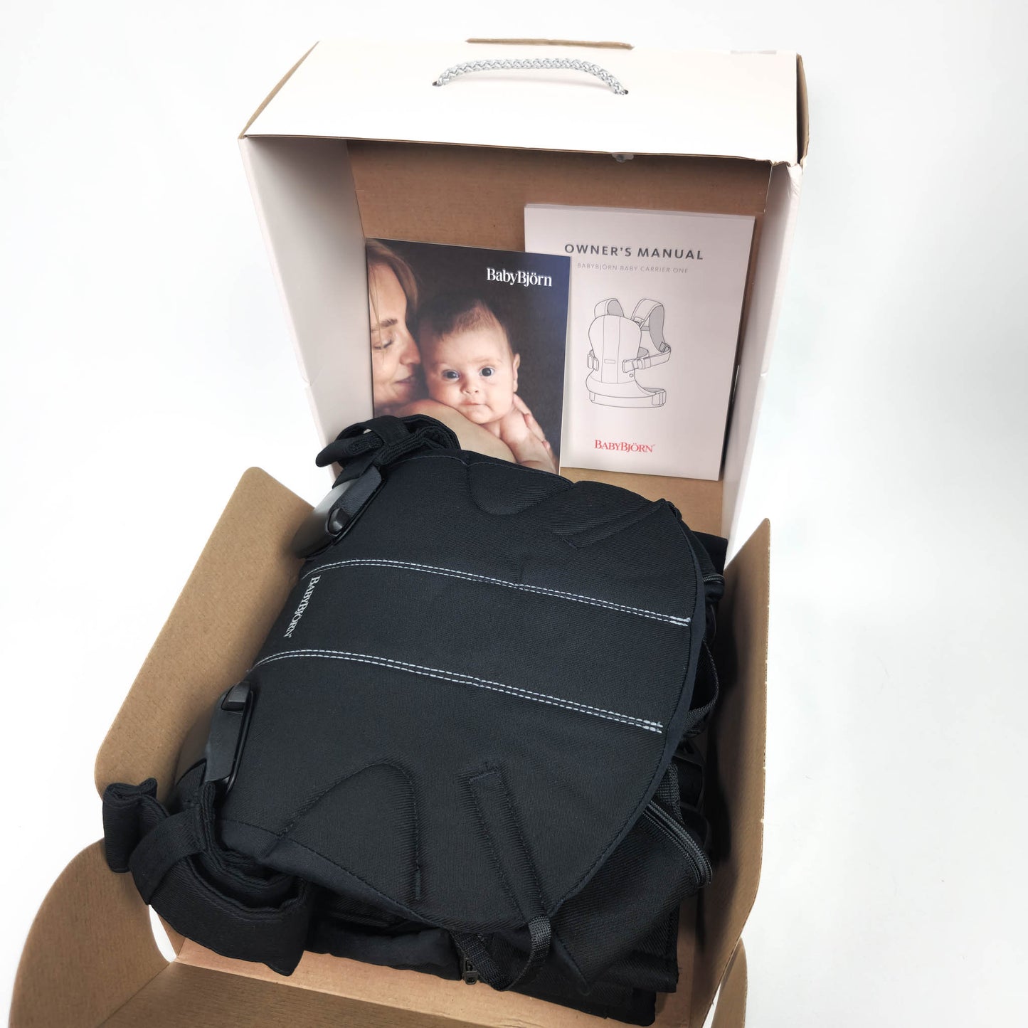 Packaging box for BABYBJÖRN Baby Carrier One in Black Cotton with image of a mother holding a baby and the carrier itself.