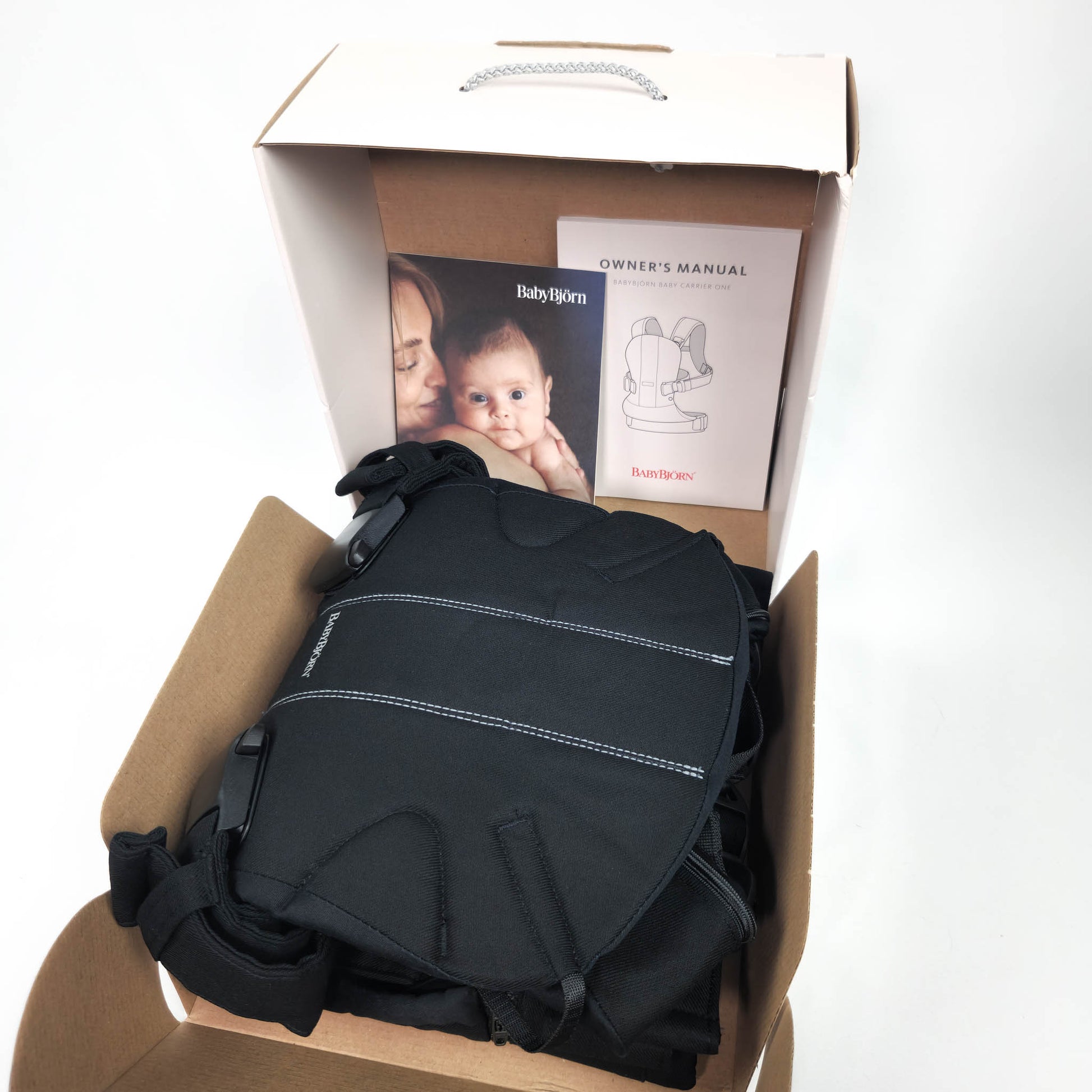 Packaging box for BABYBJÖRN Baby Carrier One in Black Cotton with image of a mother holding a baby and the carrier itself.
