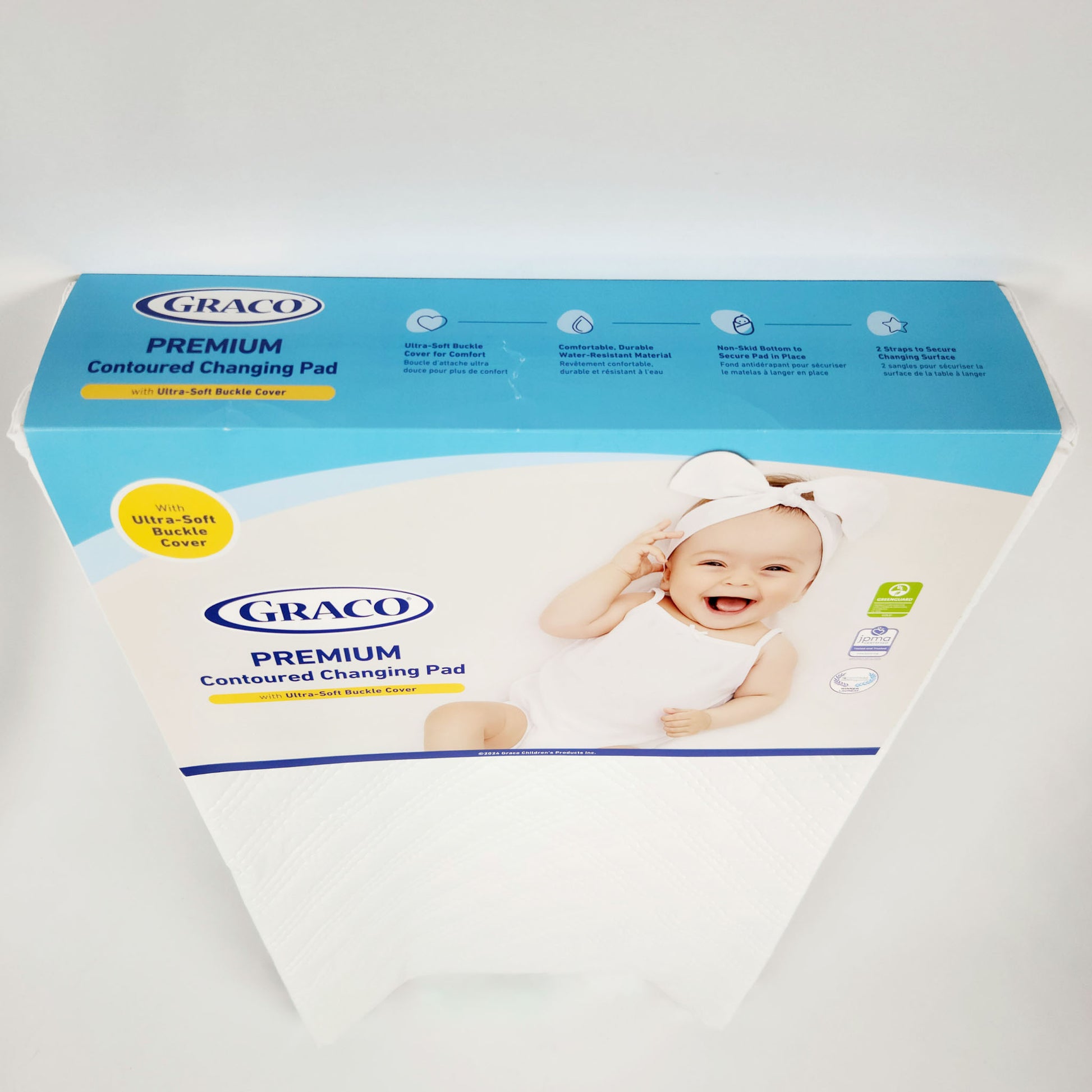 Graco Premium Contoured Changing Pad in white, with a visible blue and white packaging showing the product name and a baby image.